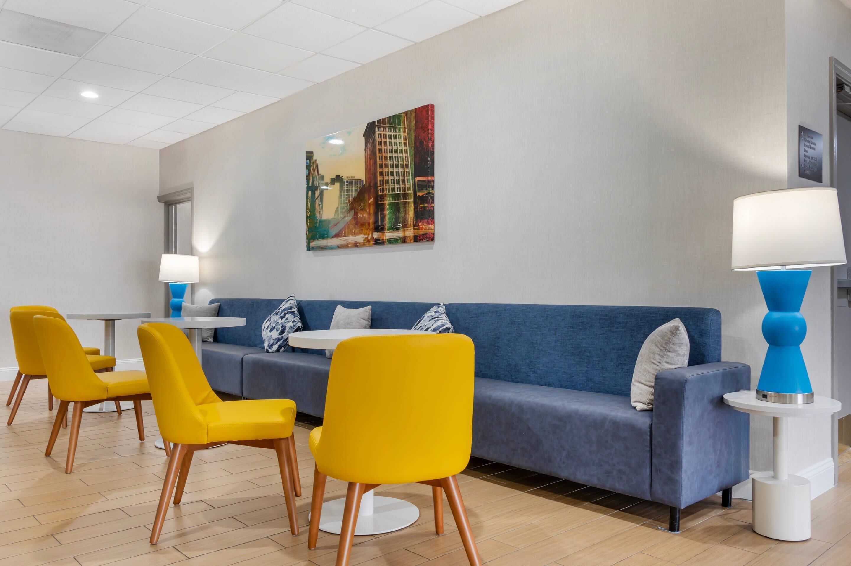 A modern hotel lobby with a blue sofa, yellow chairs, a white table, and a painting on the wall.