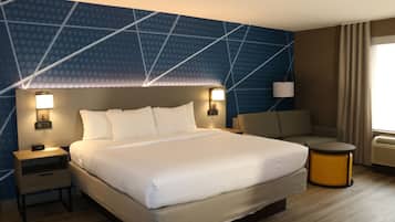 A hotel room with a large bed, two bedside tables with lamps, a sofa, and a small round table.