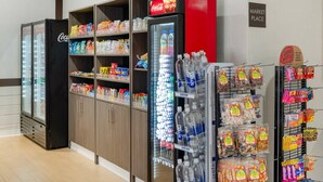 A snack and beverage vending area with a Coca-Cola refrigerator, shelves stocked with snacks and bottled water, and a sign indicating a market place. - Comfort Inn & Suites Danbury-Bethel (Danbury)