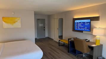 Habitación de hotel con cama, escritorio con silla, televisor montado en la pared y lámpara.