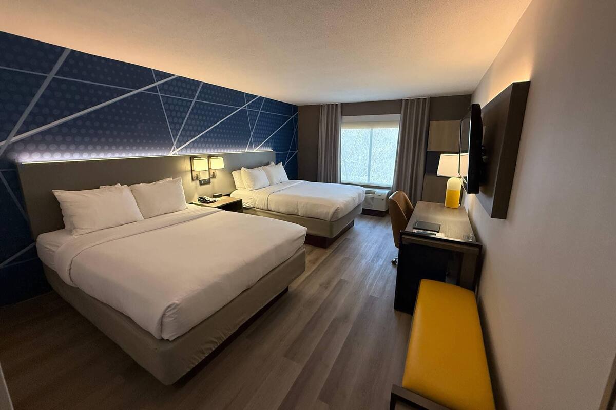 A hotel room with two beds, a desk, a chair, a TV, and a window with curtains.