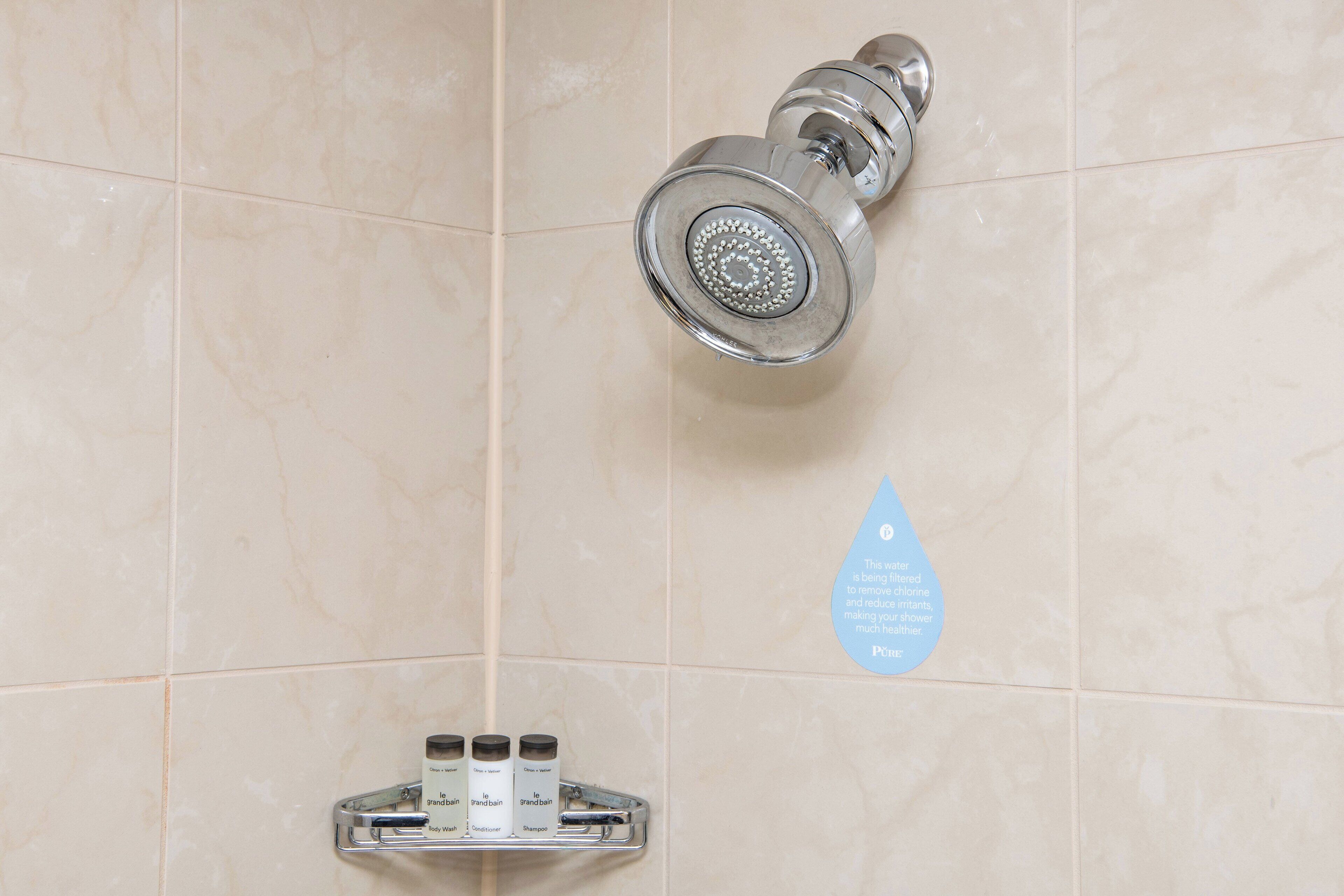 Baño con cabezal de ducha, dispensador de jabón y señal de ahorro de agua.