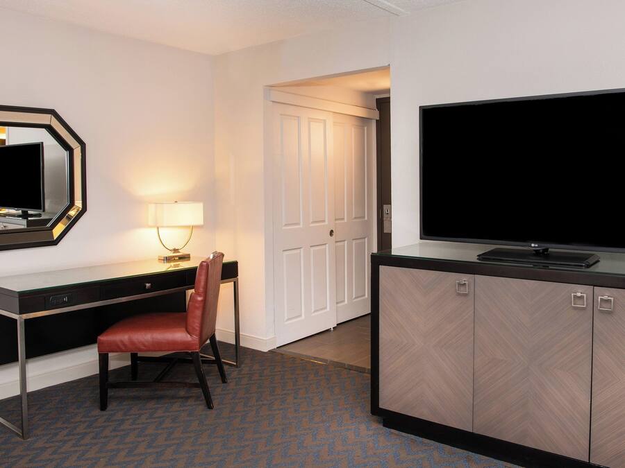 A hotel room with a desk, chair, TV, and wardrobe.