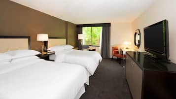 A hotel room with two beds, a desk, a television, and a window with curtains.