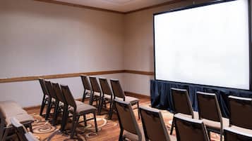 A conference room with rows of chairs, a large screen, and a carpeted floor.
