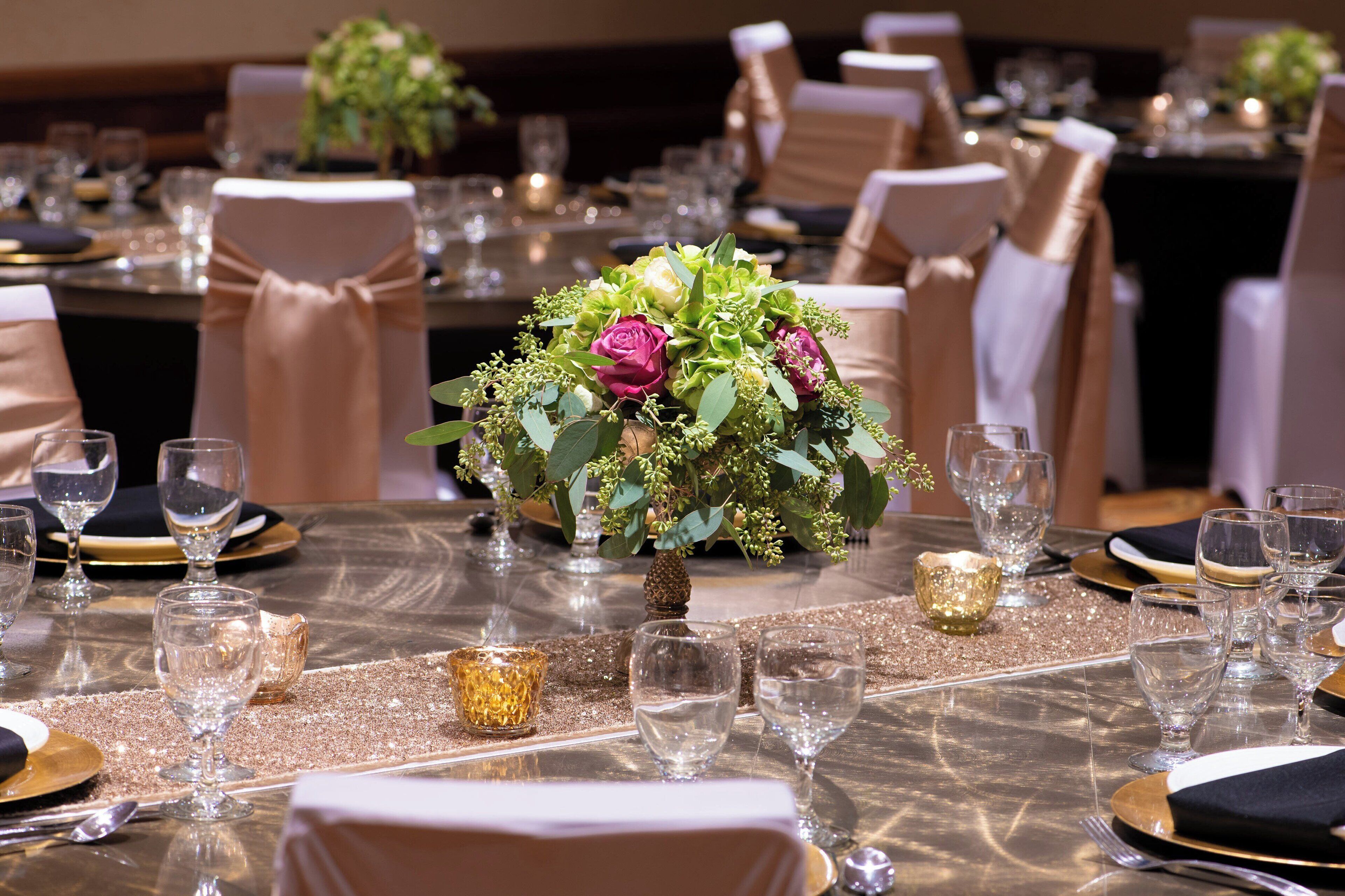A table set for a formal event with a centerpiece of flowers, clear glassware, and gold accents.