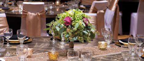 A table set for a formal event with a centerpiece of flowers, clear glassware, and gold accents.