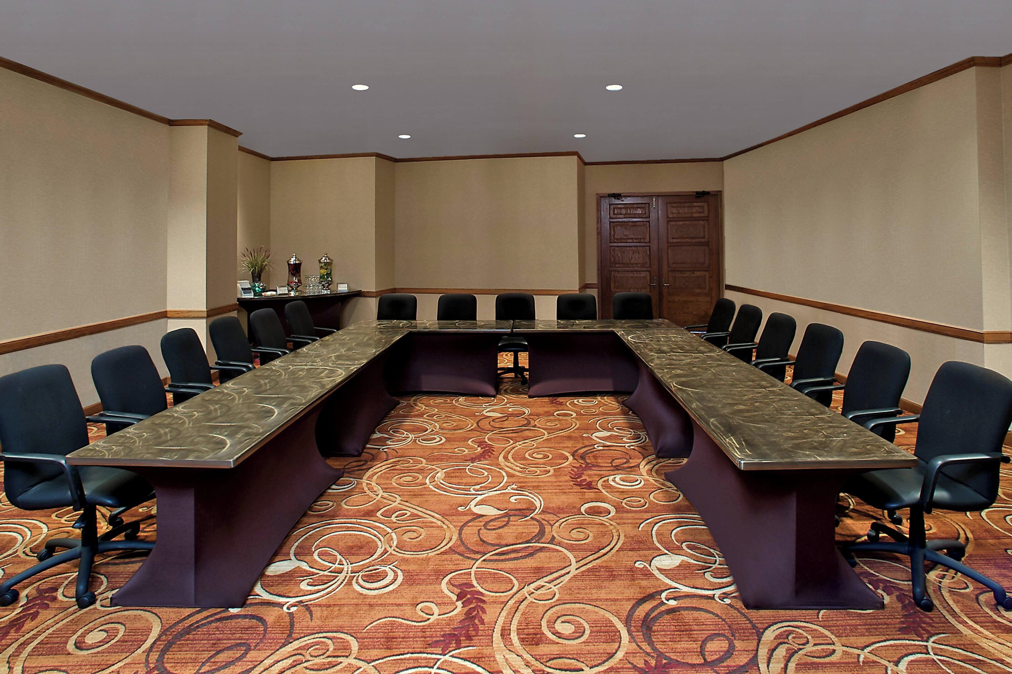 Un salón de conferencias con una larga mesa, varias sillas y piso alfombrado.