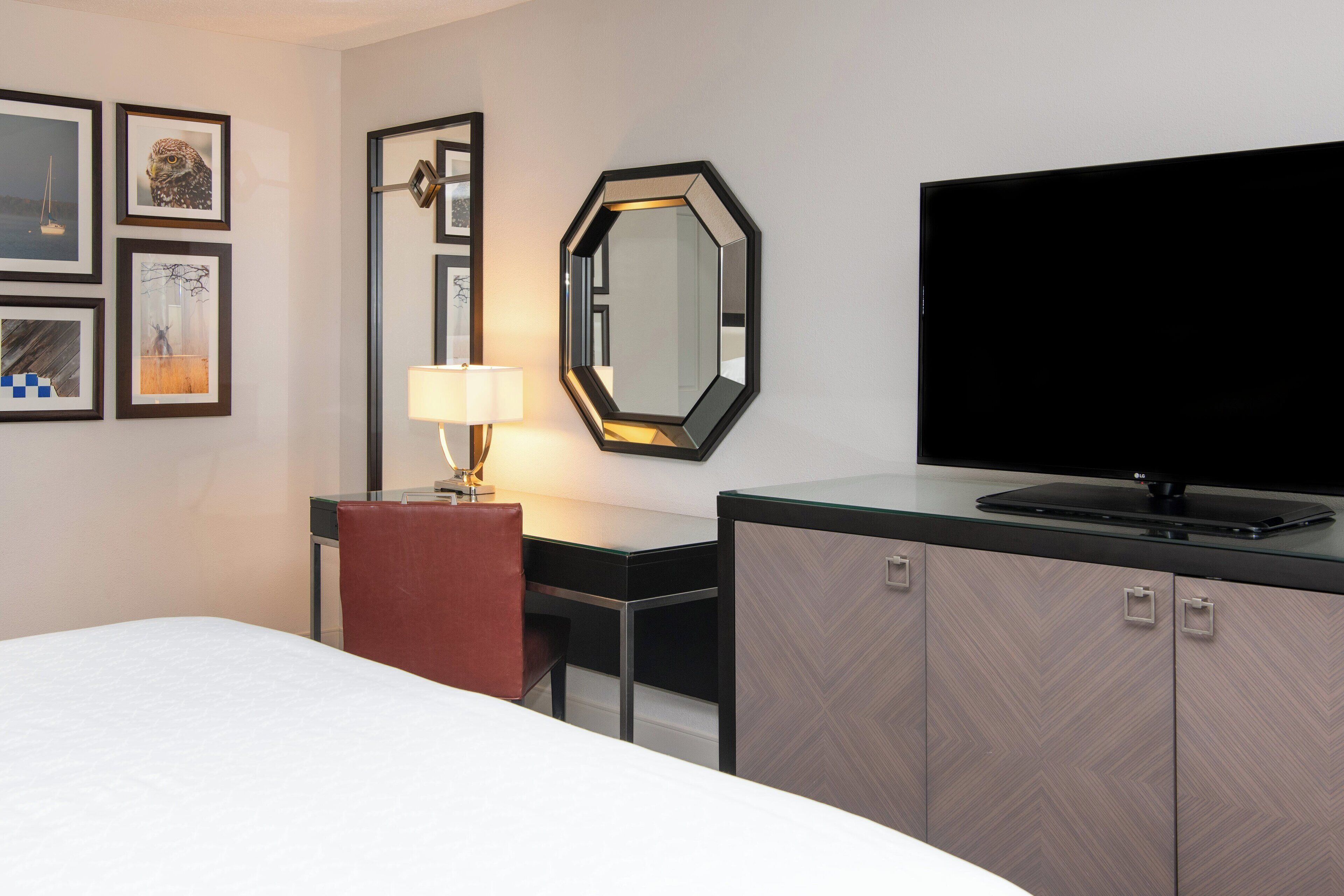 A hotel room with a bed, a desk with a lamp, a television, and a wardrobe.