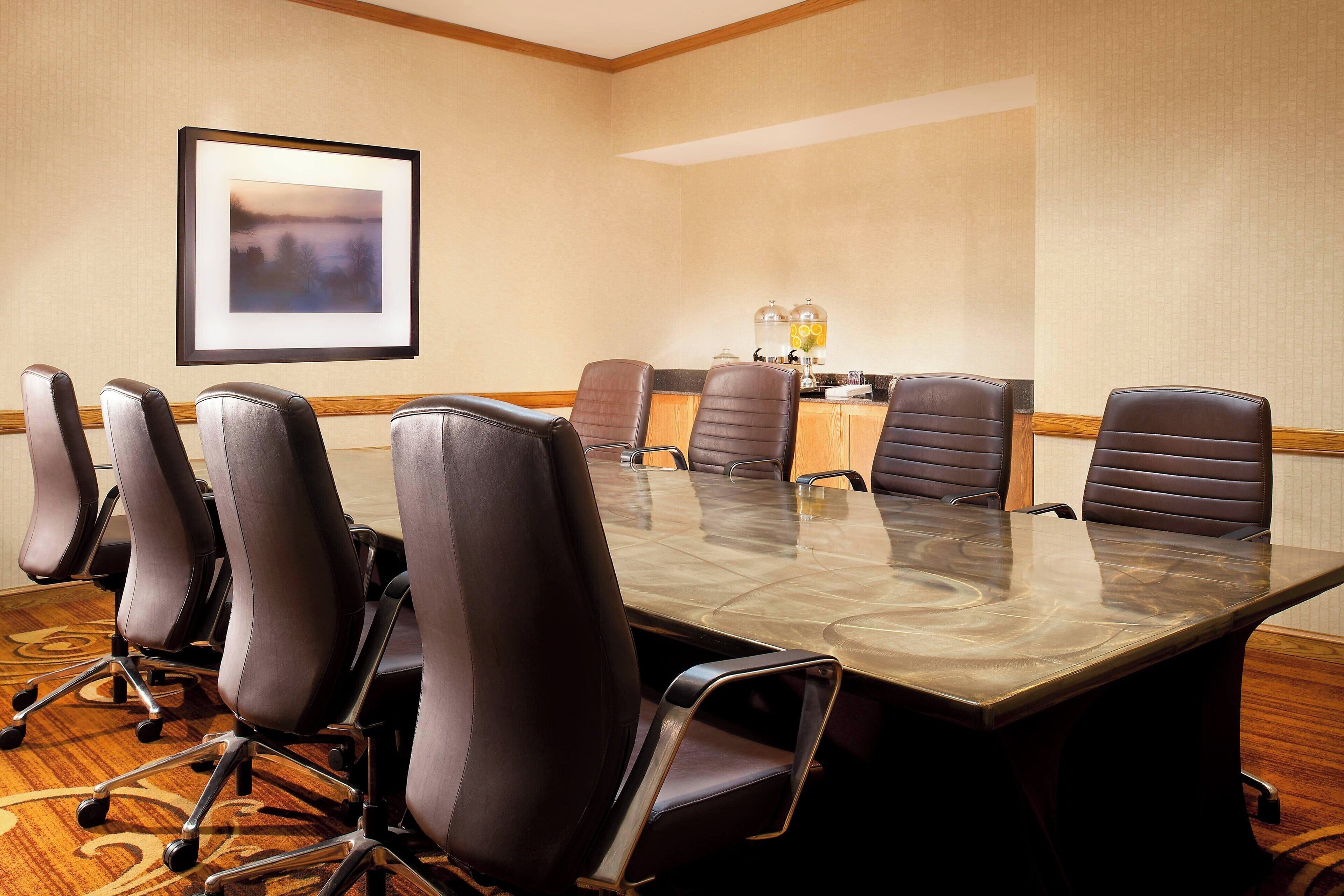 Una sala conferenze con un grande tavolo, poltrone in pelle, un quadro appeso al muro e un tavolino con un vaso e candele.