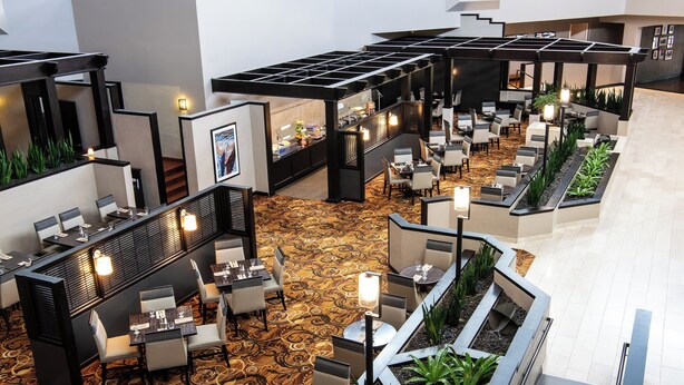 A spacious hotel lobby with multiple seating areas, a central bar, and a patterned carpet.