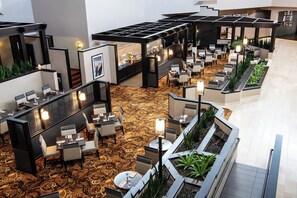 Un espacioso vestíbulo de hotel con varias zonas de estar, un bar central y una alfombra estampada.