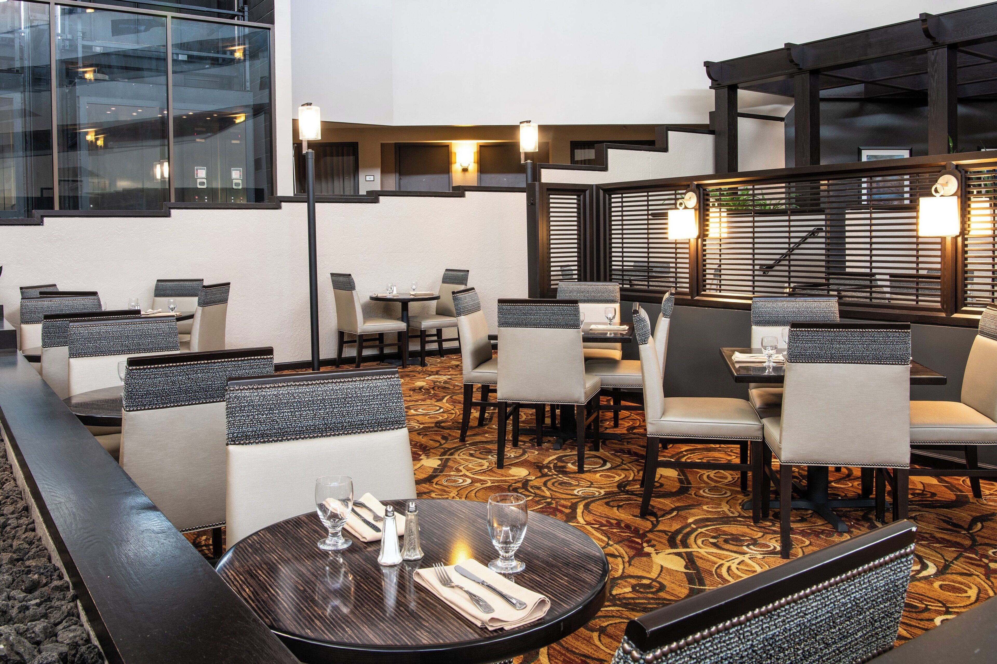A hotel dining area with round tables, cushioned chairs, and a patterned carpet.