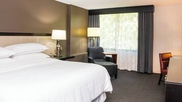 A hotel room with a large bed, a chair, a desk, and a window with curtains.