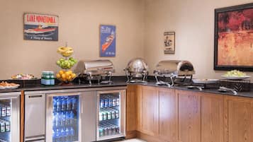 A buffet setup with a refrigerator, a fruit bowl, and various food items.