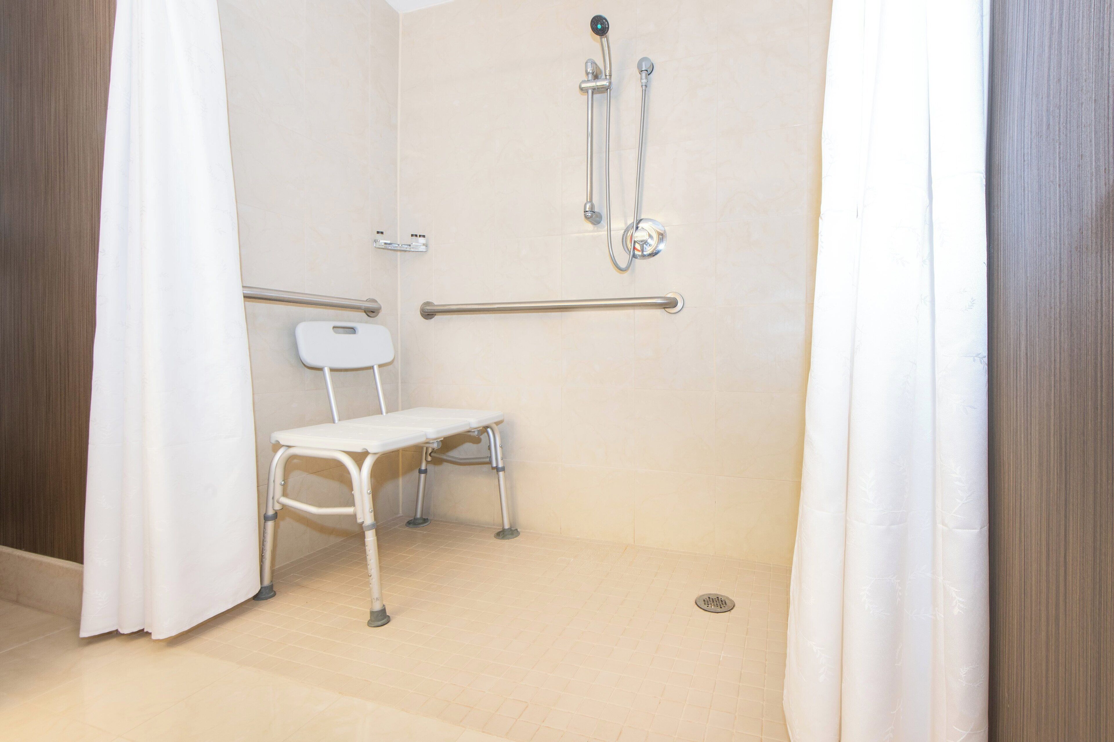 Un baño con ducha, barras de apoyo, inodoro y banco accesible en silla de ruedas.
