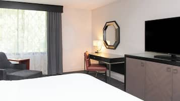 Una habitación de hotel con cama, escritorio, silla, televisor y ventana con cortinas.