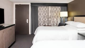 Una habitación de hotel con cama, escritorio, televisor y cortina estampada.
