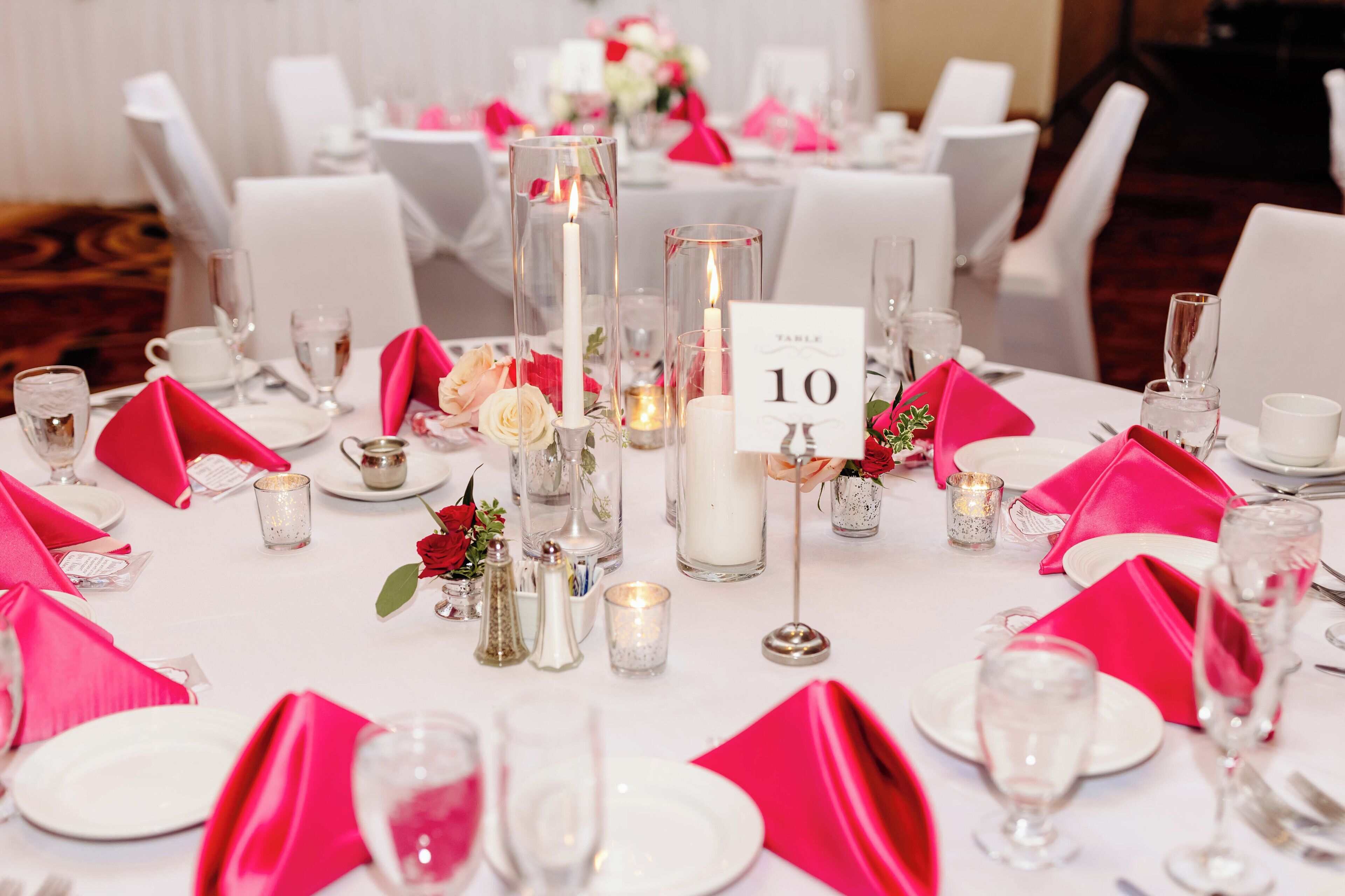 A table set with white plates, pink napkins, and clear glassware, with a number sign indicating table 10.