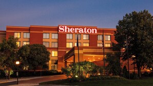 A Sheraton hotel with a modern design, featuring a prominent sign, multiple windows, and a parking lot.