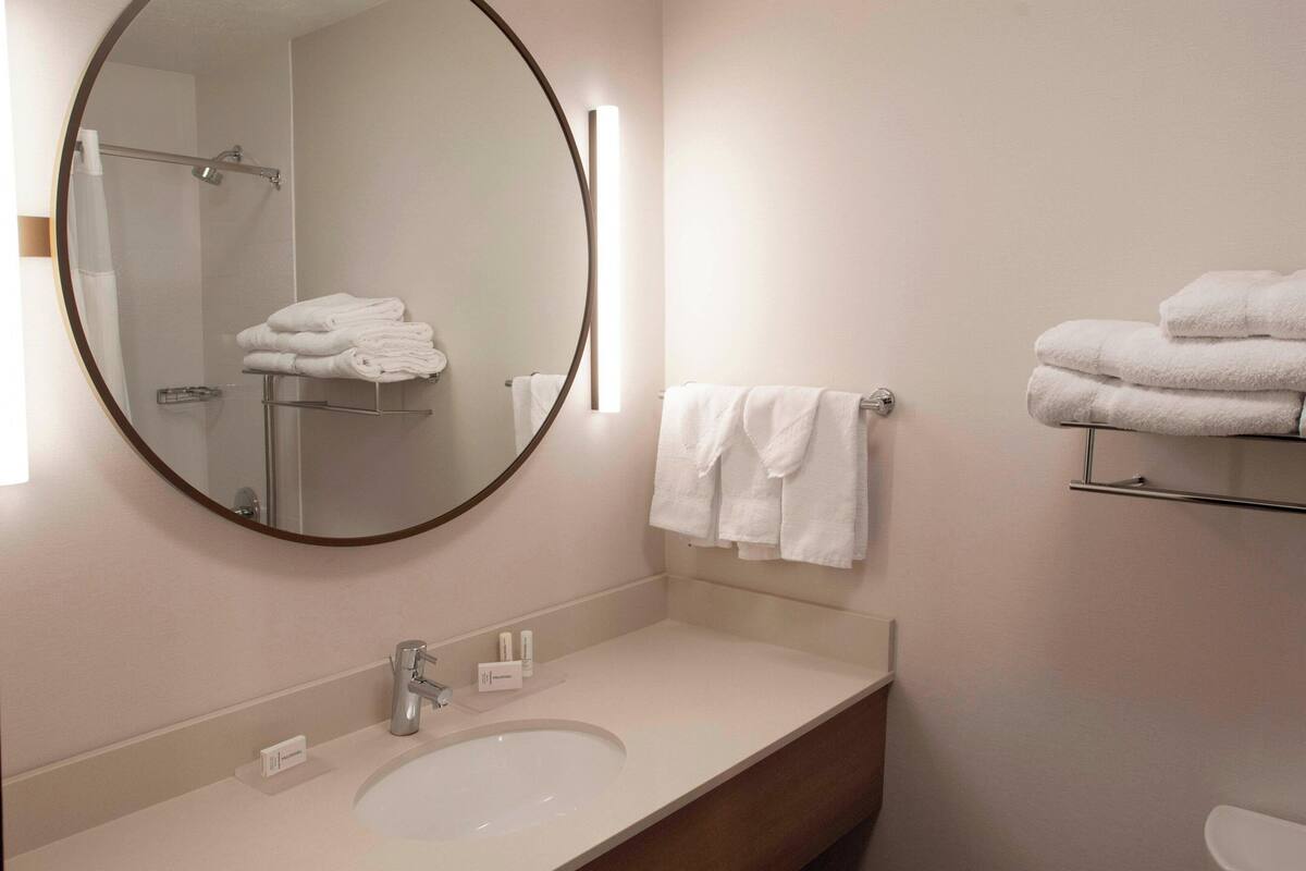 A modern bathroom with a round mirror, a sink, a towel rack, and a toilet.