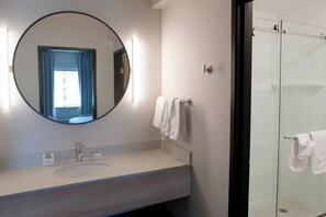 A modern bathroom with a round mirror, a sink, and a glass shower enclosure. - Fairfield Inn & Suites by Marriott Spokane Valley (Spokane Valley)