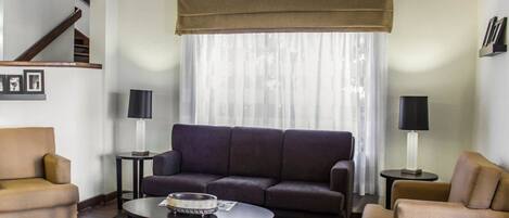 A modern living room with a sofa, armchairs, a coffee table, and two lamps. A staircase is visible in the background.