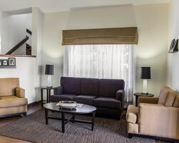 A modern living room with a sofa, armchairs, a coffee table, and two lamps. A staircase is visible in the background.