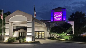 A Sleep Inn & Suites by Choice Hotels building with a prominent purple sign, a flag, and a well-lit entrance. - Sleep Inn & Suites Spring Lake - Fayetteville near Fort Bragg (Spring Lake)