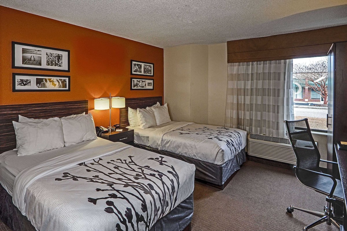 Habitación de hotel con dos camas, un escritorio, una silla y una ventana con cortinas.