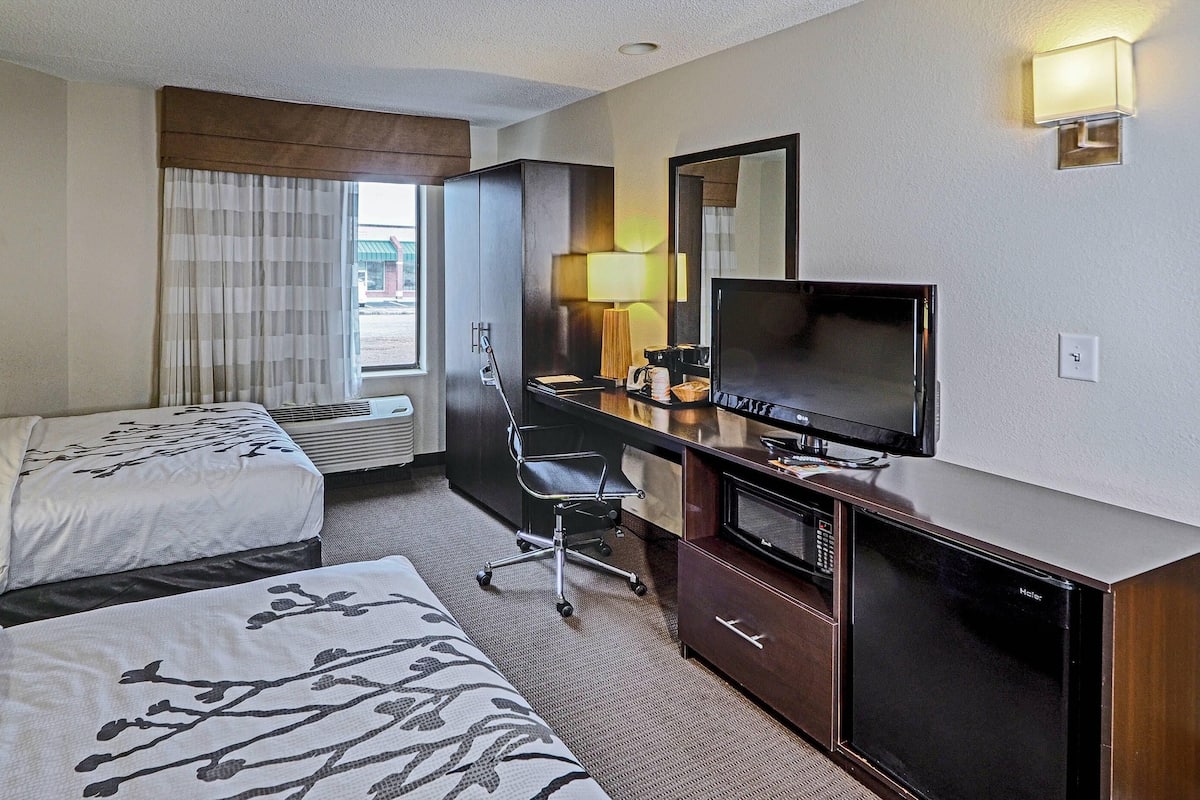 Habitación de hotel con dos camas, un escritorio con televisor, una lámpara de escritorio, una silla y un minibar.