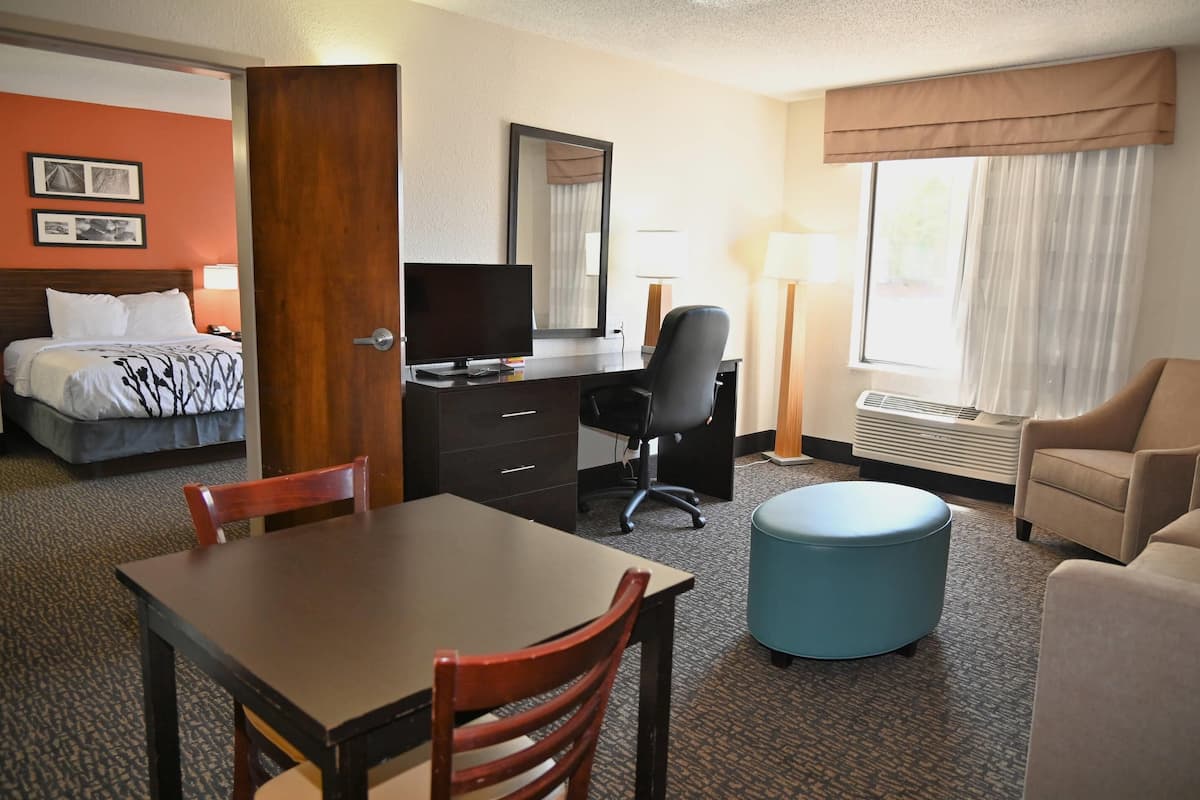 Una habitación de hotel con cama, escritorio, silla, reposapiés y ventana con cortinas.