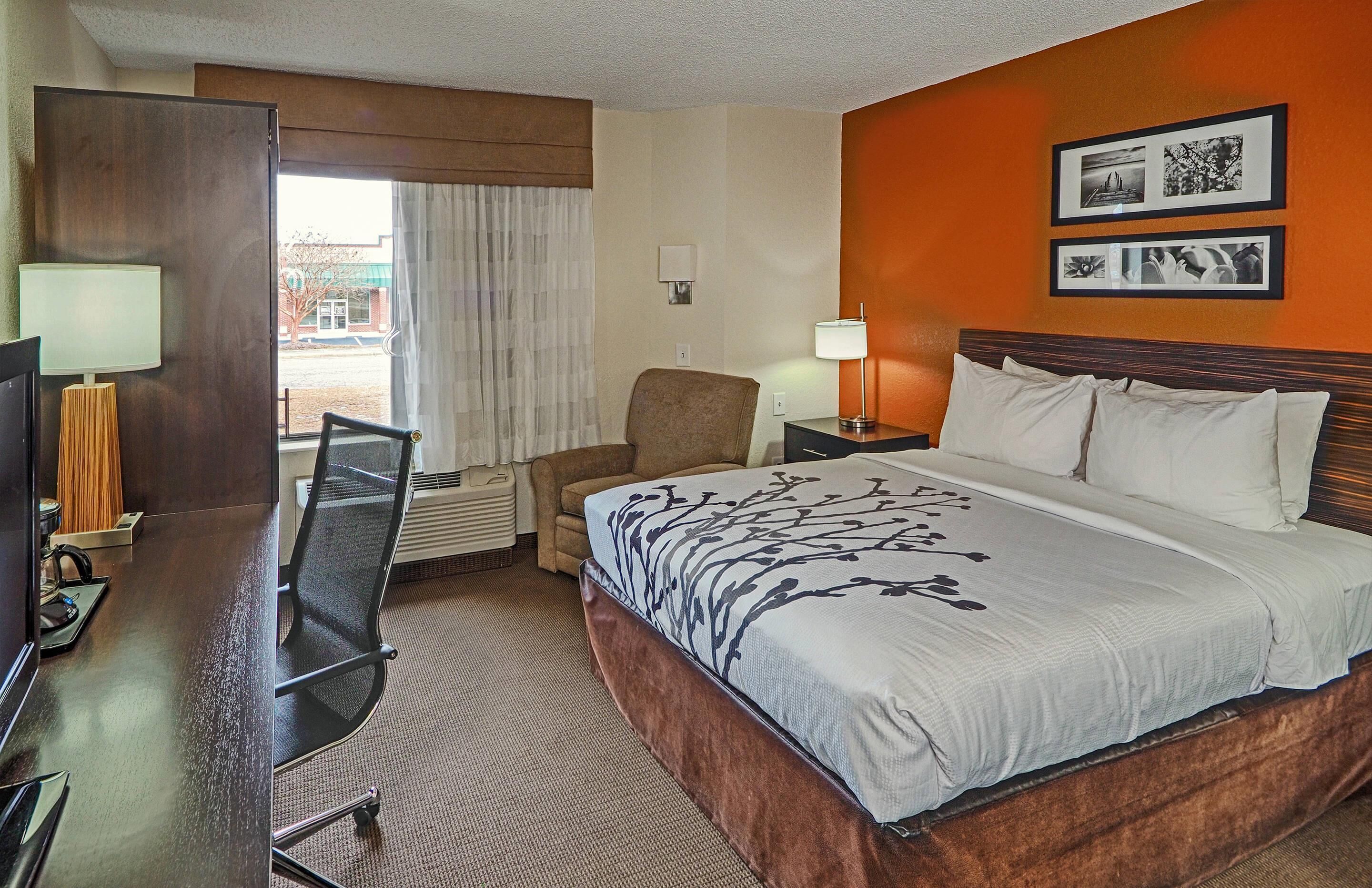 A hotel room with a large bed, a desk with a chair, a TV, and a window with curtains.