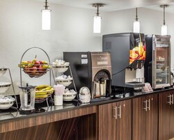 A coffee station with a coffee machine, fruit bowls, and a beverage dispenser.