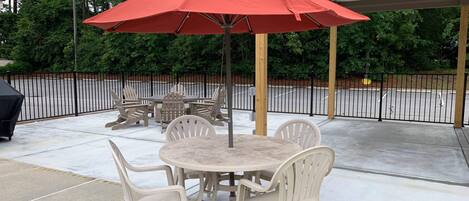 An outdoor patio with a round table and four chairs, a red umbrella, and a grill.