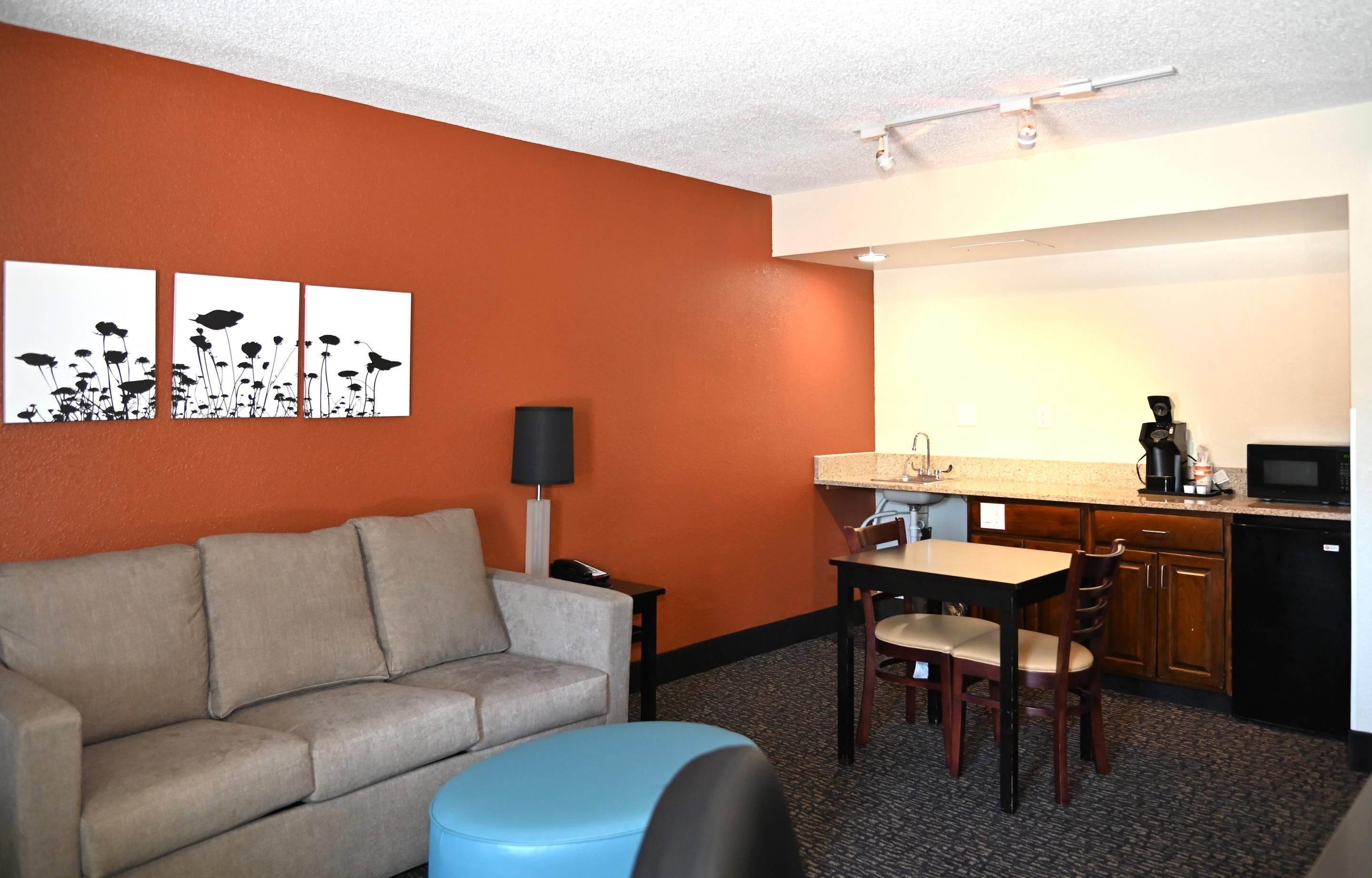 A hotel room with a sofa, a dining table with chairs, a kitchenette, and three wall art pieces.