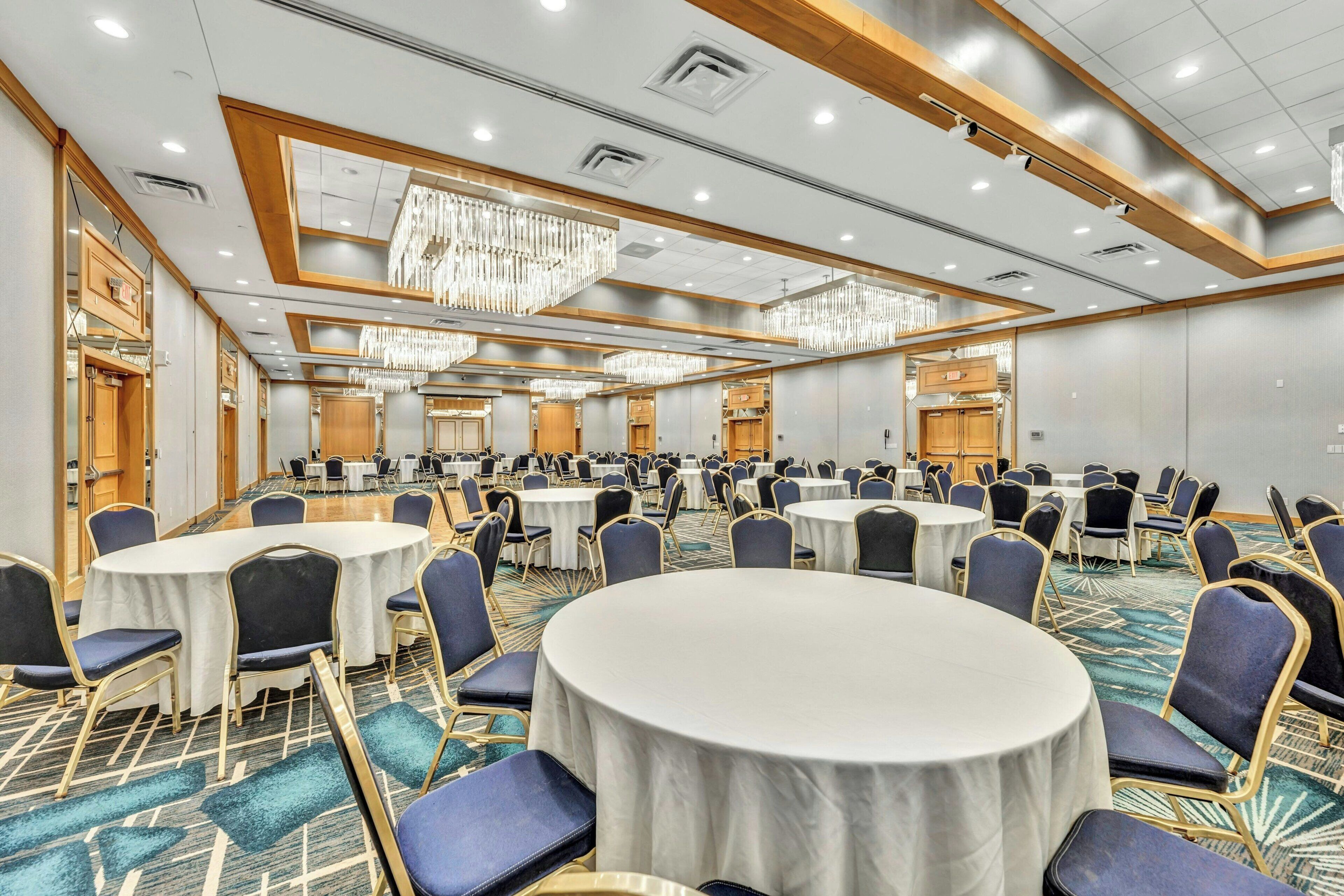 Een ruime congreszaal met ronde tafels en stoelen, houten lambrisering en kroonluchters.