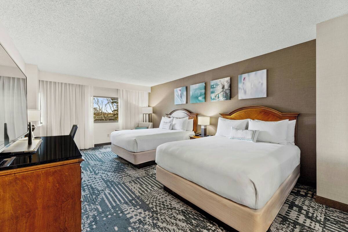 Habitación de hotel con dos camas, un escritorio y un ventanal grande.