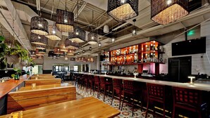 Un ristorante con tavoli e sedie in legno, lampade di vimini appese e una zona bar con scaffali pieni di bottiglie.