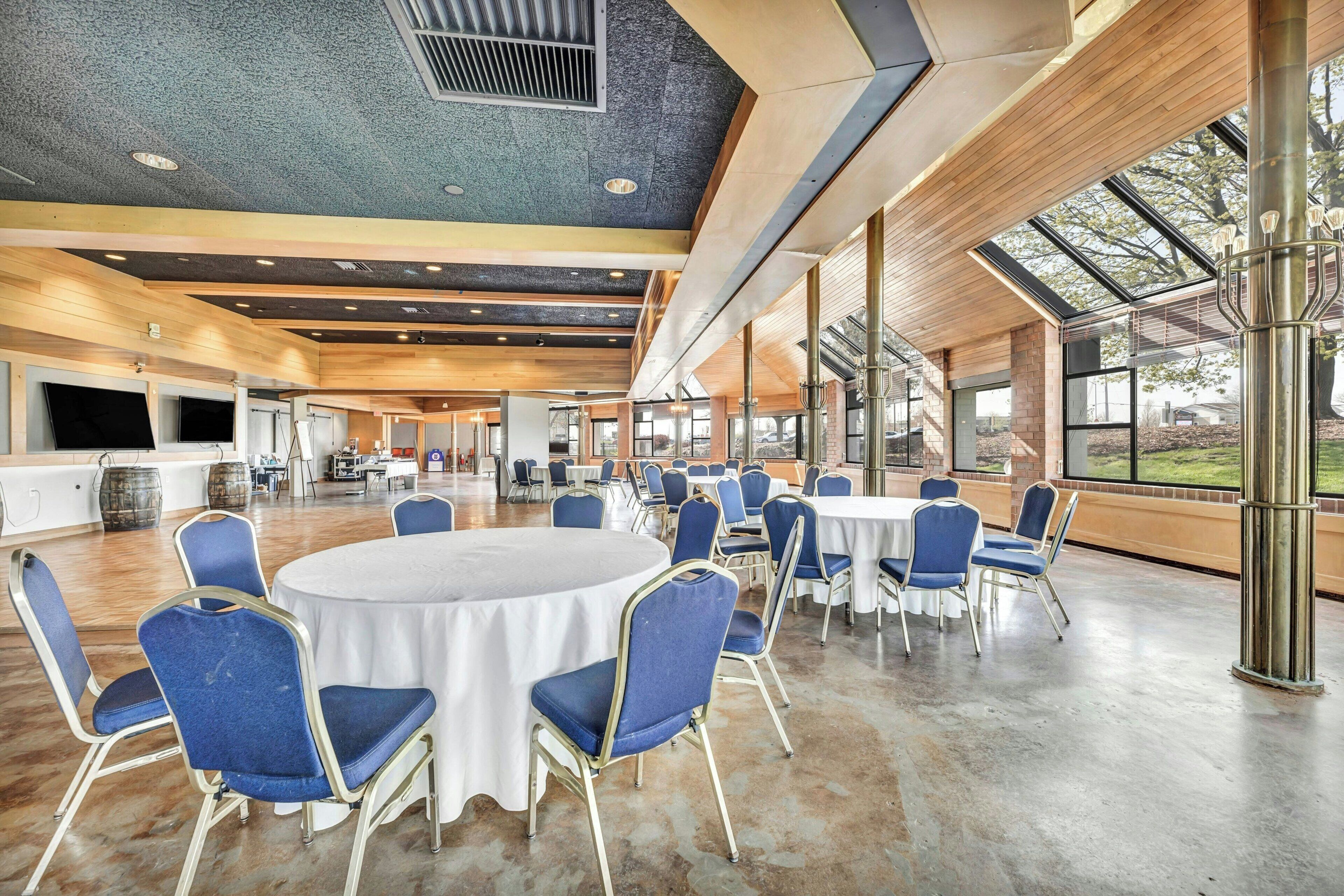 A spacious indoor area with round tables and blue chairs, large windows, and a modern ceiling design.