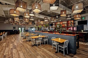 Un restaurant doté de nombreuses tables et chaises, d’un bar et de luminaires suspendus en osier.
