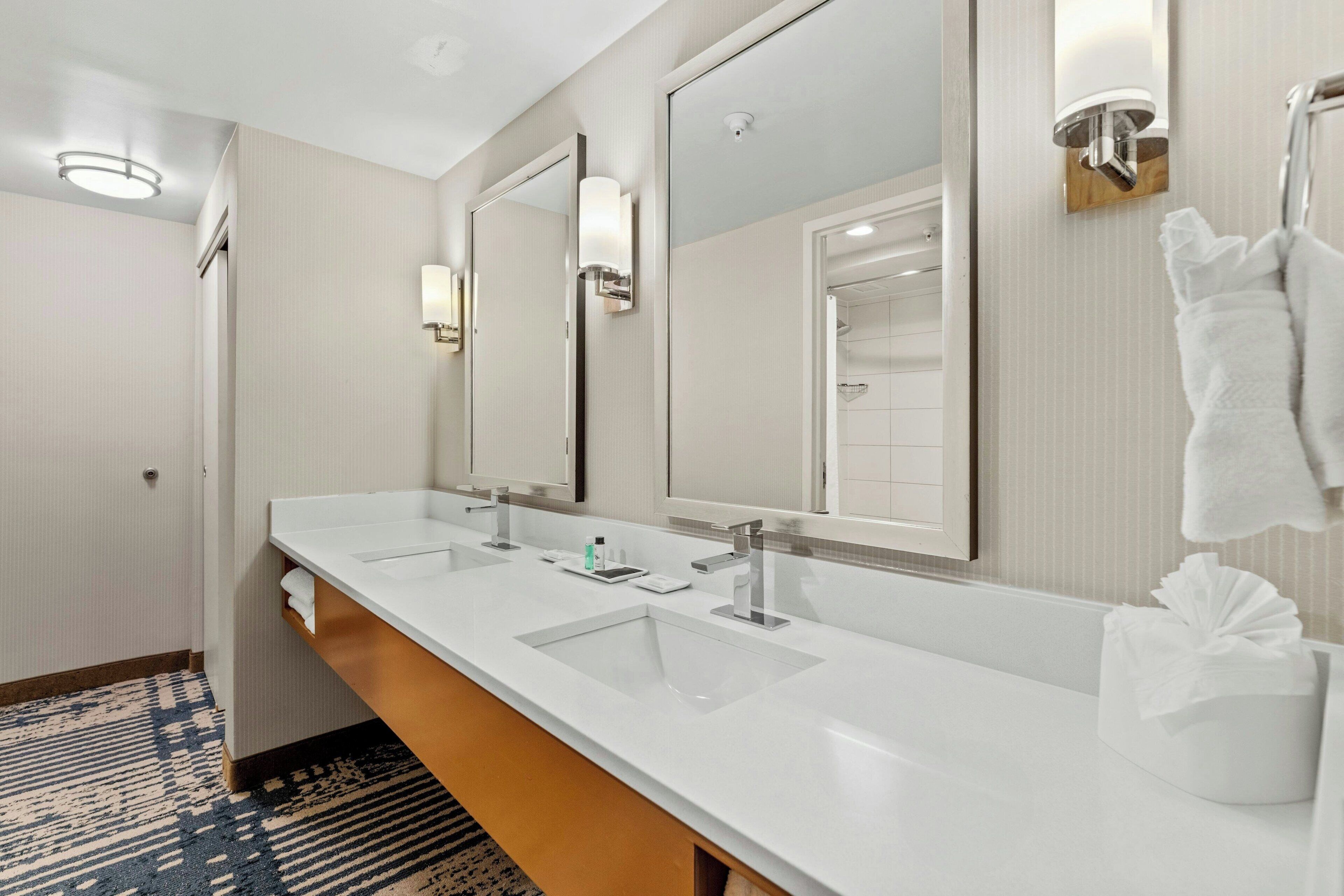 A hotel bathroom with two sinks, a large mirror, and a towel rack.