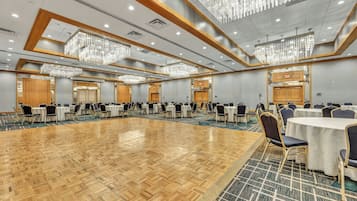 Un amplio salón de conferencias con múltiples mesas y sillas, suelo de madera y modernos candelabros.