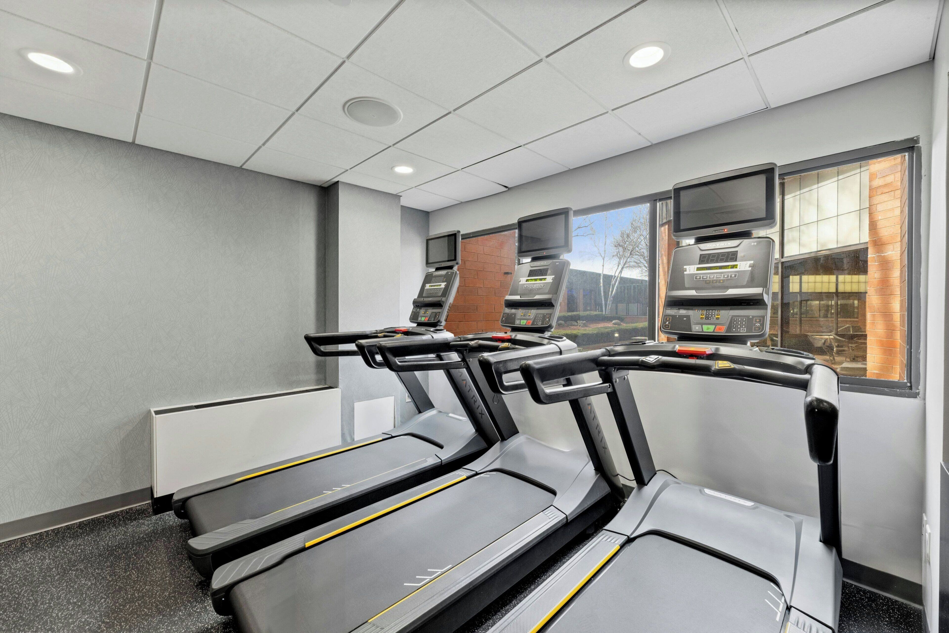 A fitness room with treadmills, a brick wall, and a window with a view of the outside.