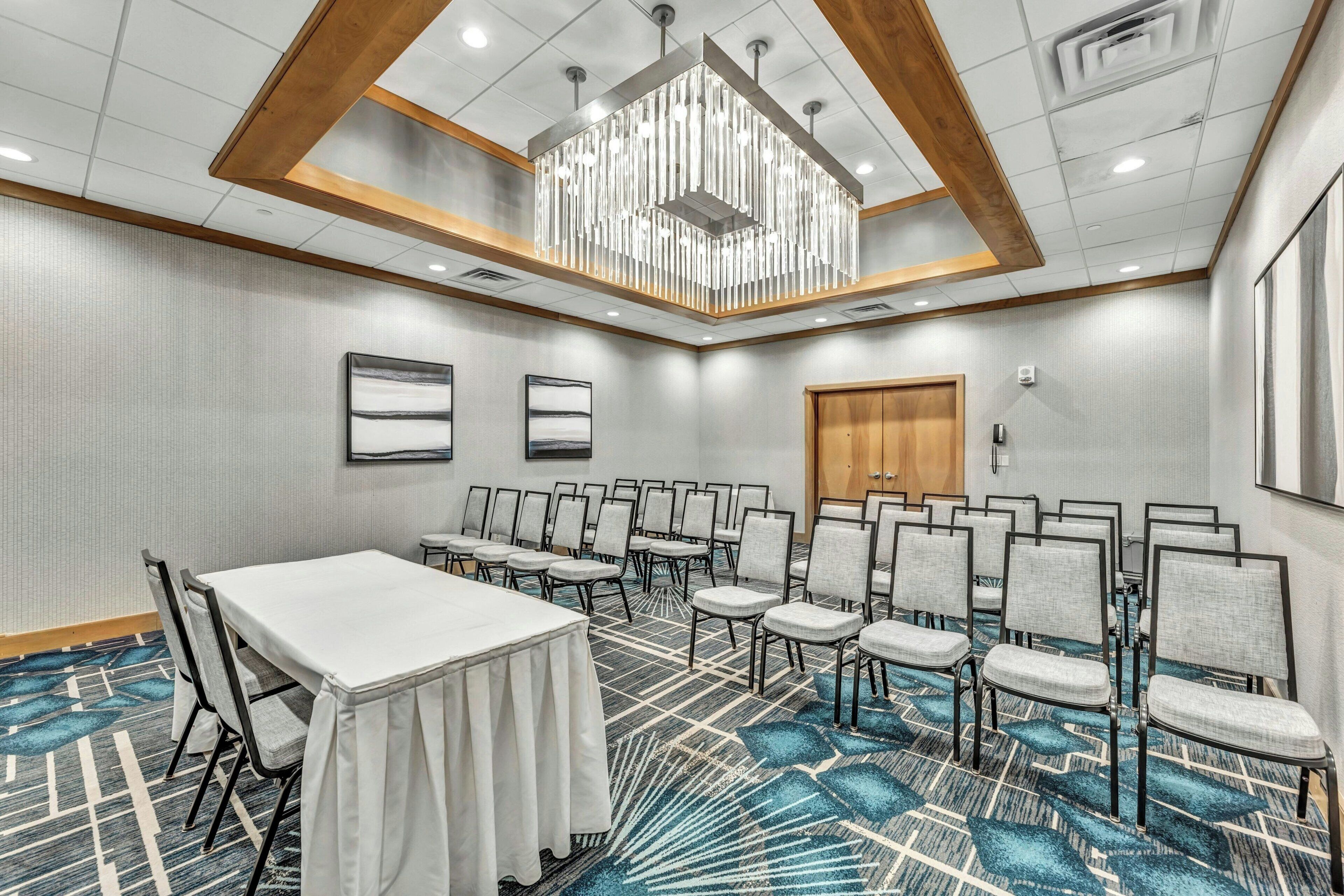 A conference room with a long table and rows of chairs, a chandelier, and a patterned carpet.