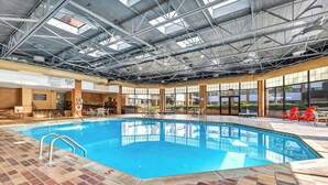Una piscina interna con pavimento in piastrelle chiare, struttura del tetto in metallo e vista sull'esterno attraverso ampie finestre.