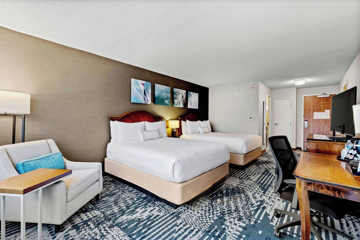 Habitación de hotel con dos camas, un escritorio, una silla, un televisor y una obra de arte en la pared.