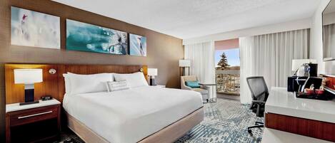A hotel room with a large bed, a desk, a chair, a nightstand, and artwork on the wall.