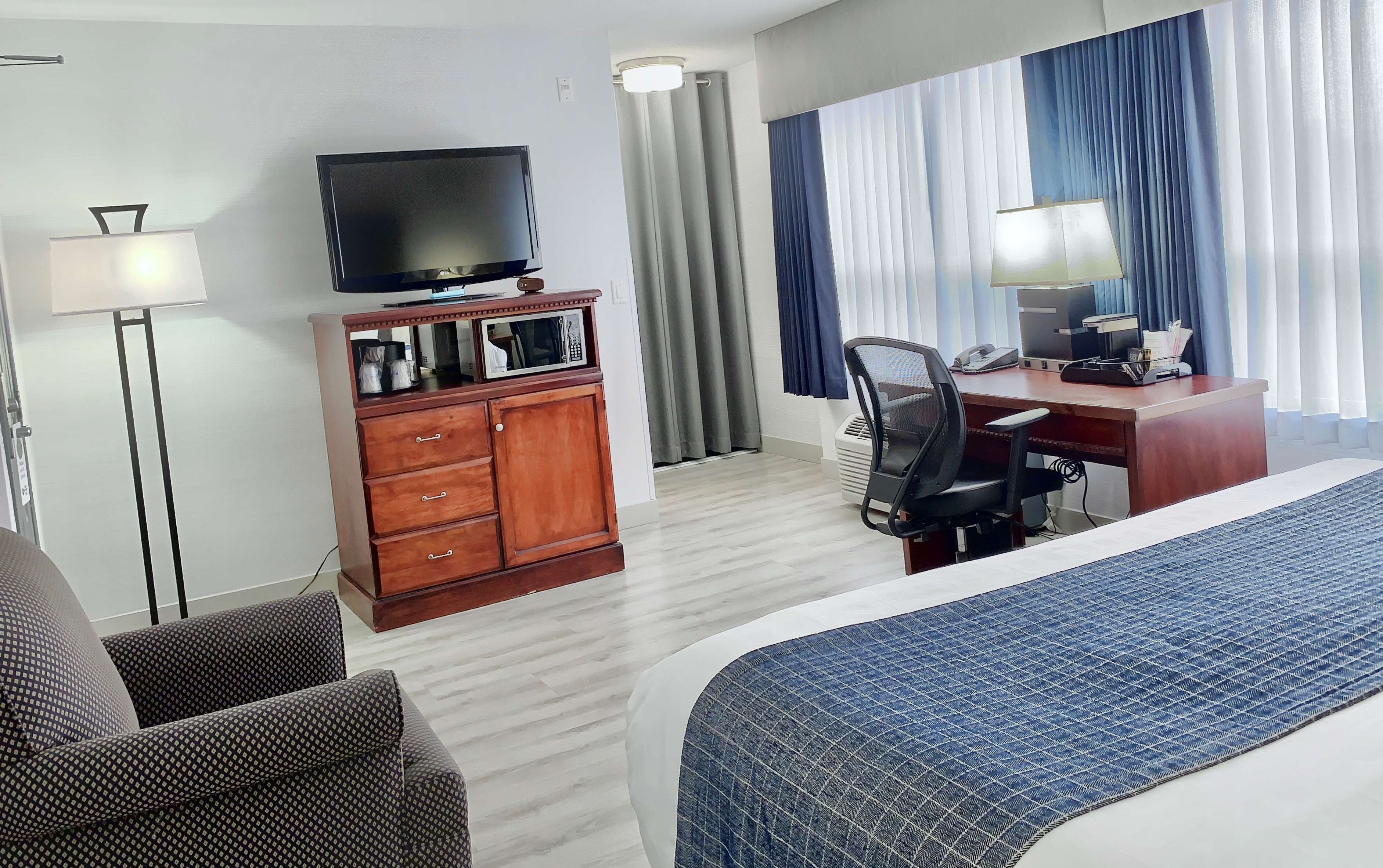 Habitación de hotel con cama, escritorio, silla, televisor, armario y lámpara.