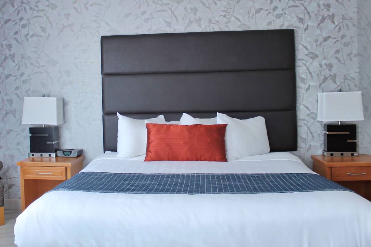 A hotel room with a large bed, two bedside tables with lamps, a chair, and a patterned wallpaper.